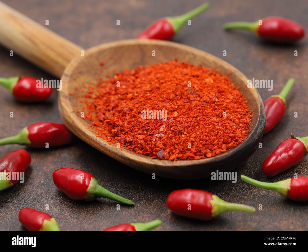 red pepper flakes on wooden spoon on table with small spicy thai chillis Stock Photo