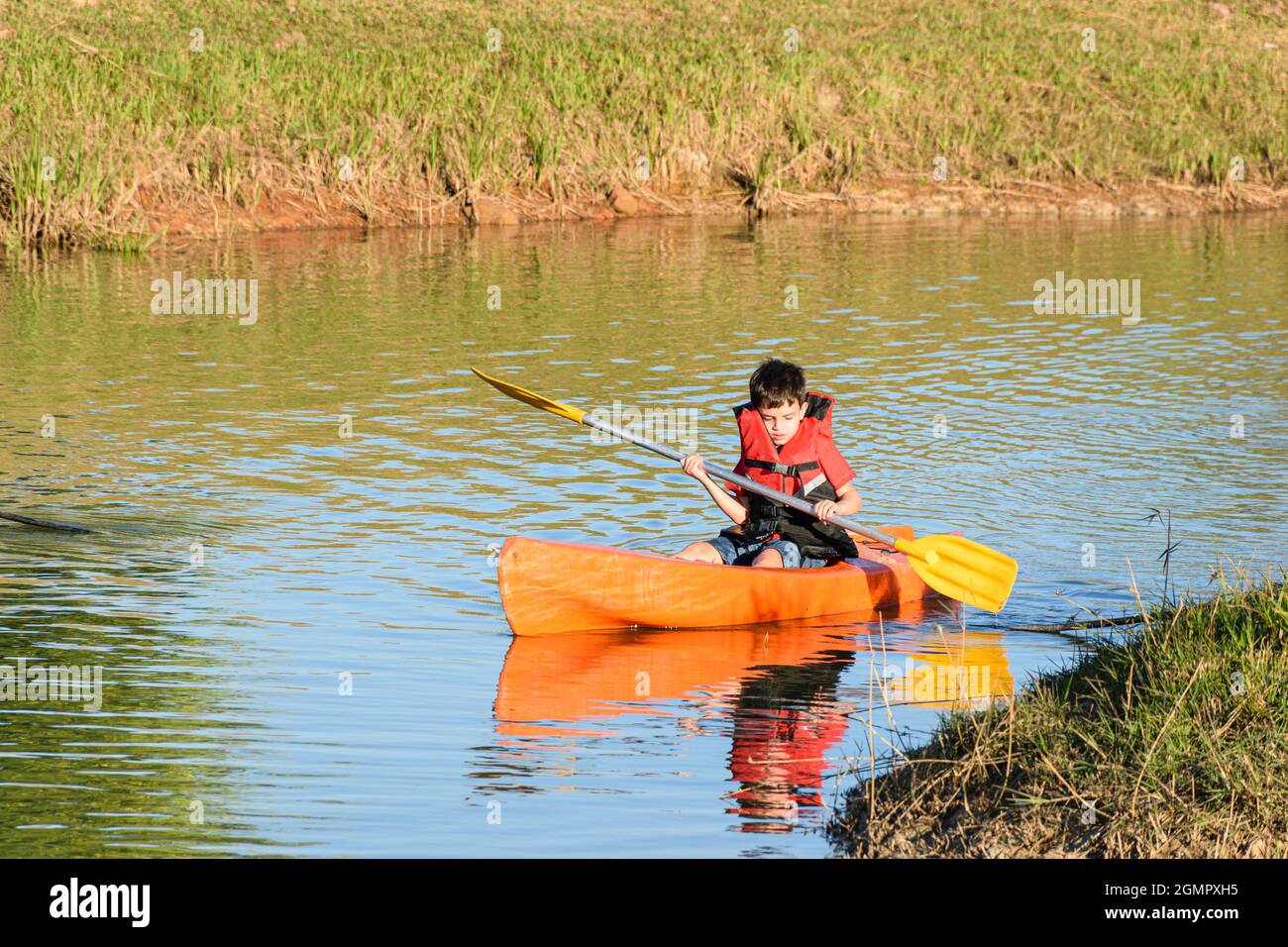 8 year old Brazilian child sailing in a kayak in a small river on a sunny day. Stock Photo