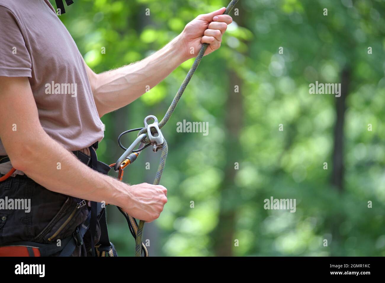 Man belays his partner climber with belaying device and rope. Climber's