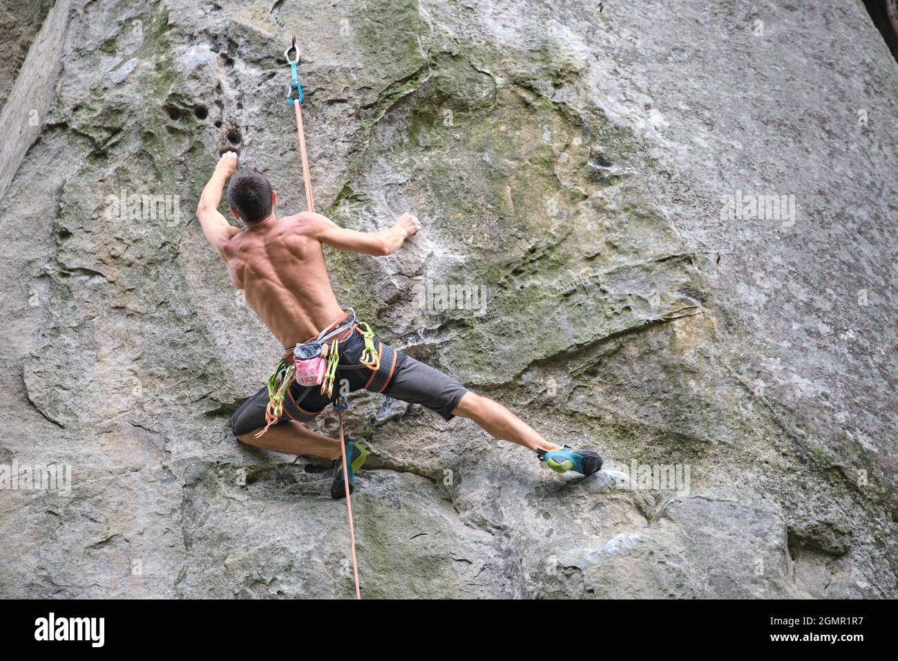 Determined climber clambering up steep wall of rocky mountain ...
