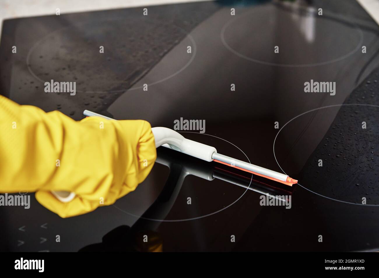 Cleaning induction stove. Woman in yellow rubber gloves cleans kitchen