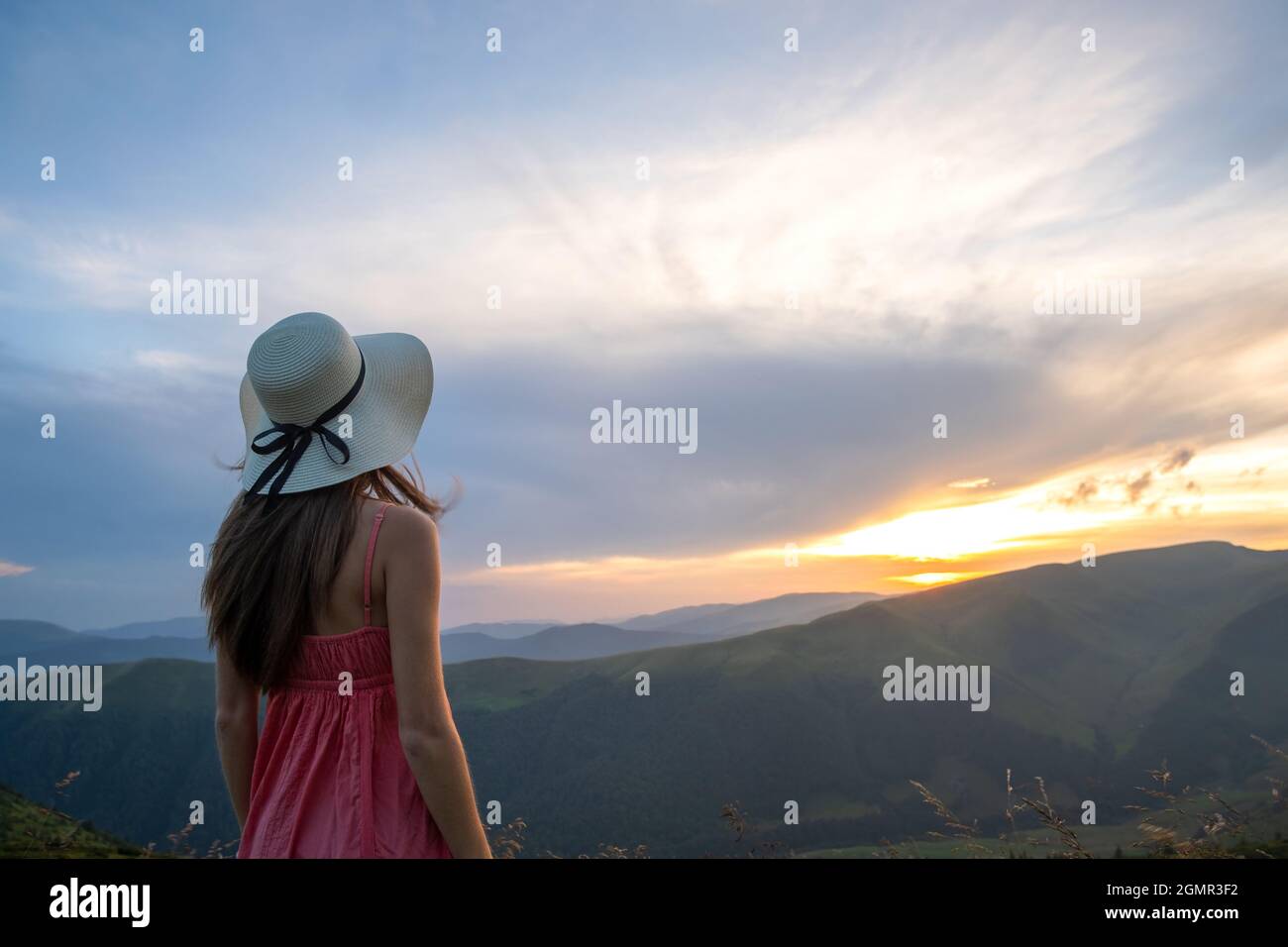 Young woman in red dress standing on grassy field on a windy evening in ...