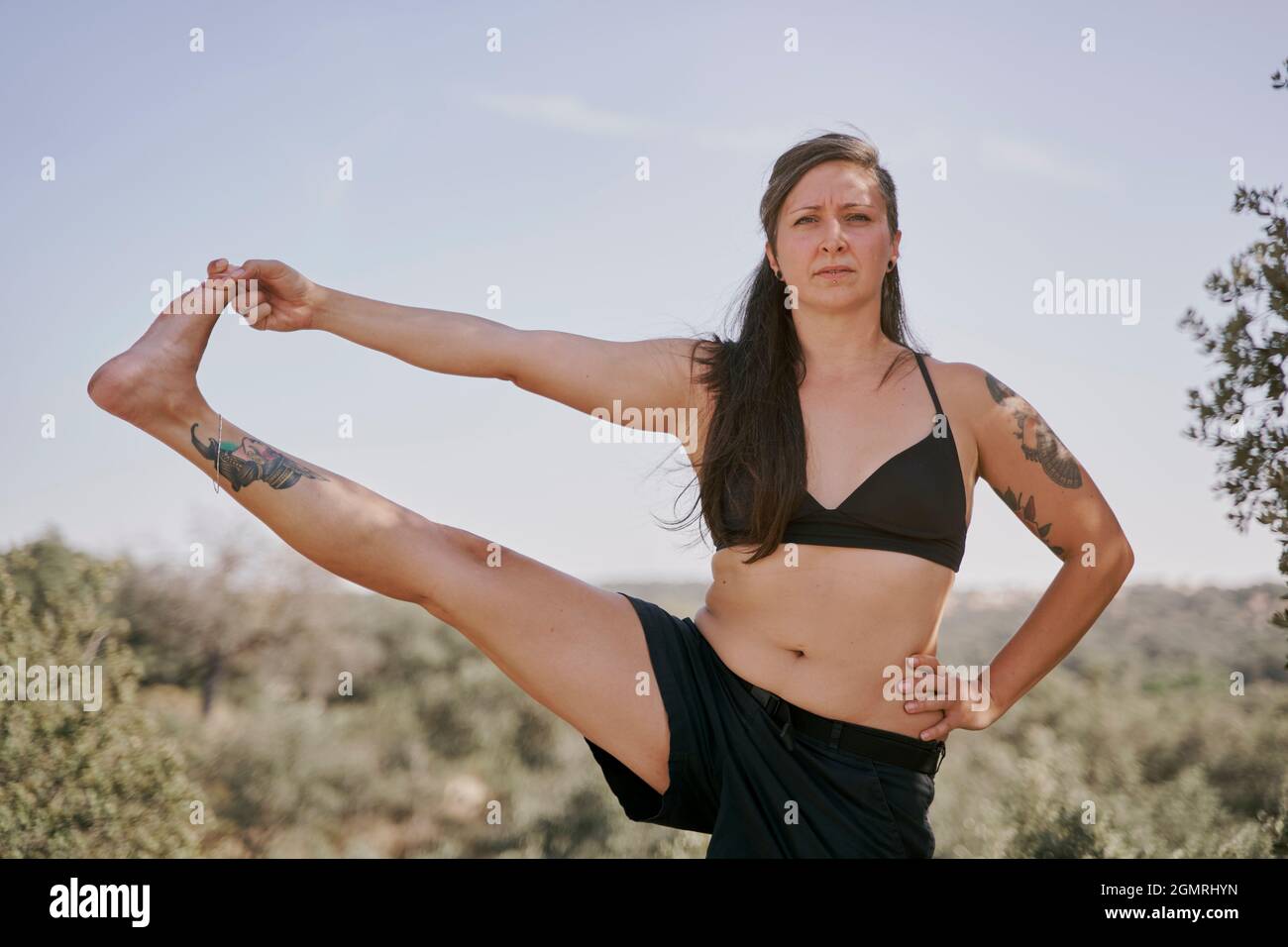 Healthy woman practising yoga in nature. Sporty woman in yoga posture with one leg raised. Utthita Hasta Padangusthasana Stock Photo