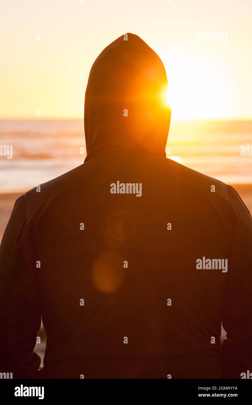 A man standing alone on a beach looking out towards the sea and the ...