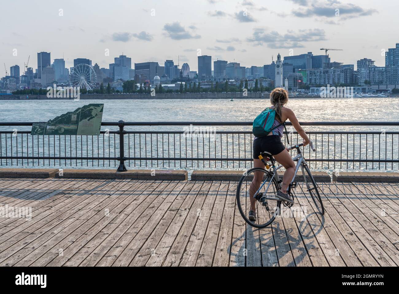 Montreal, Quebec, Canada - August 3 2021 : A woman rides a bicycle and watching the sunset in Jean-Drapeau park maritime shuttle landing stage. Saint Stock Photo