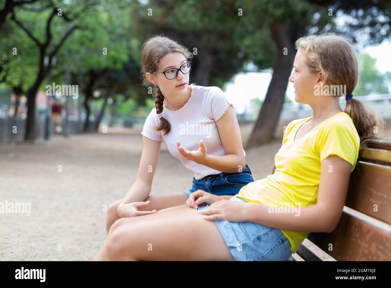 Two girls sitting on bench in park and laughing Stock Photo - Alamy