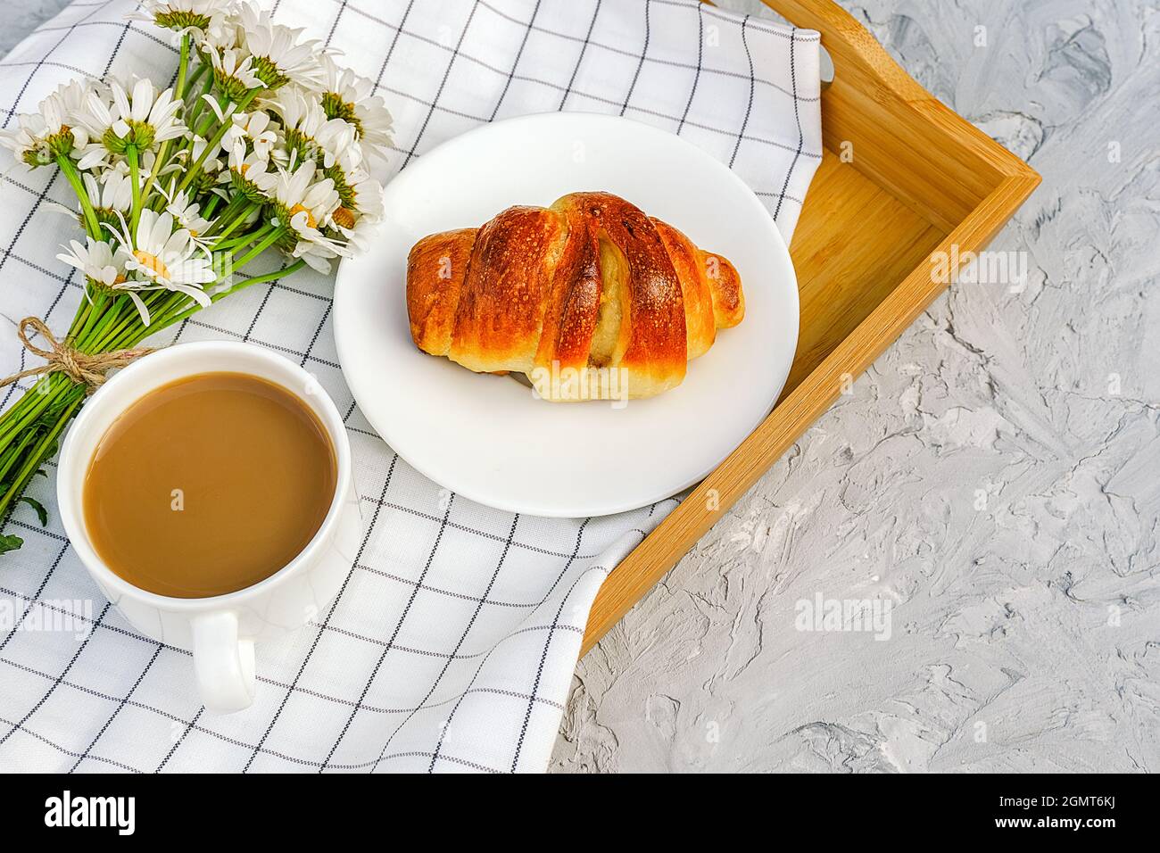 Cup of coffee with milk, freshly baked croissant, checkered napkin and camomile flowers on wooden tray on gray stone table. Concept Good morning Top v Stock Photo