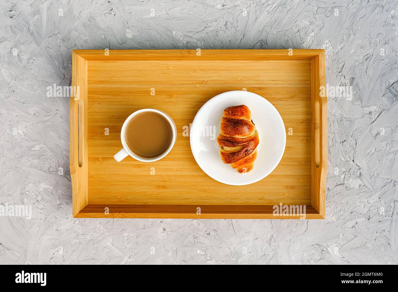 Cup of coffee with milk and freshly baked croissant on wooden tray on gray stone table. Concept Good morning Top view. Stock Photo