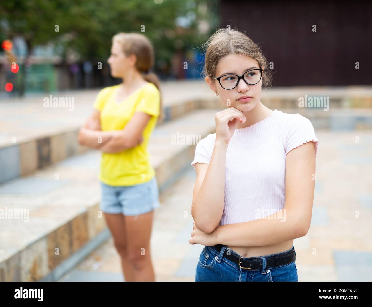 Offended girl turned away from her friend after quarrel on street Stock Photo