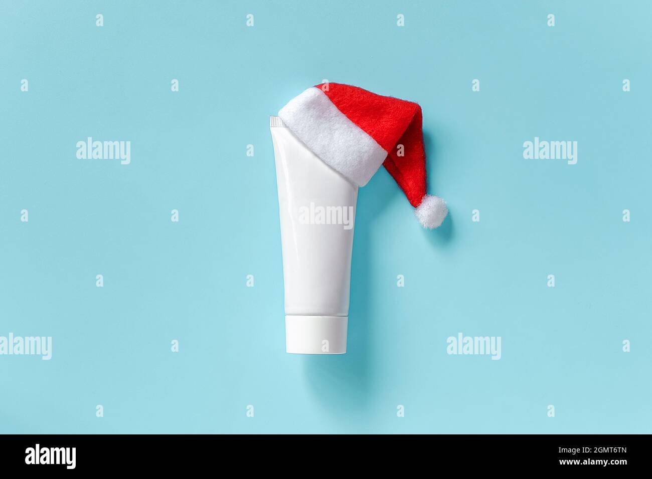 Cosmetic, medical white tube for cream, ointment or other product in red Santa Claus hat on blue background. Concept winter skin and body care or xmas Stock Photo