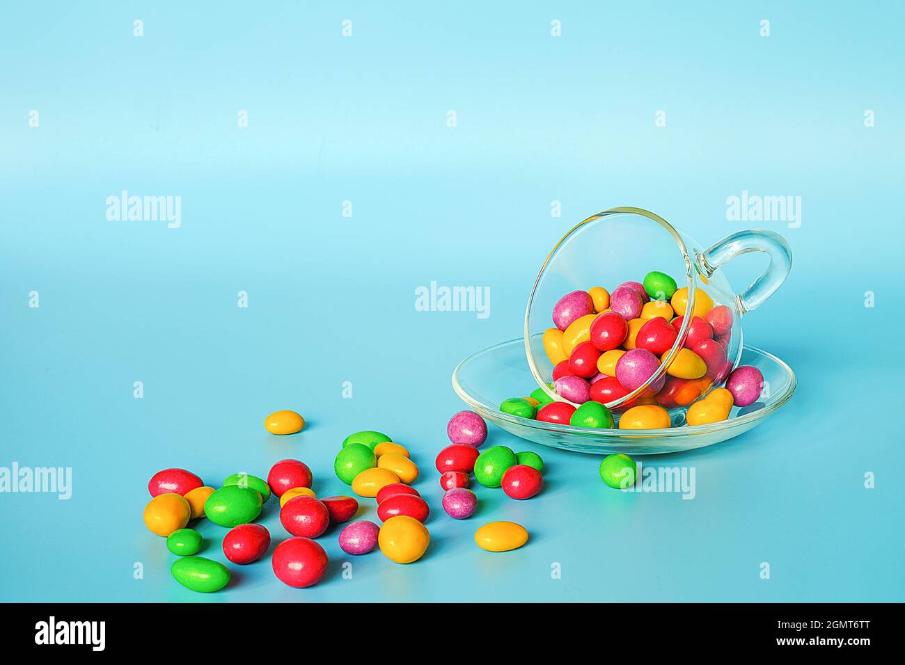 Colored glazed candy beans. Glass mug on saucer and scattered colorful