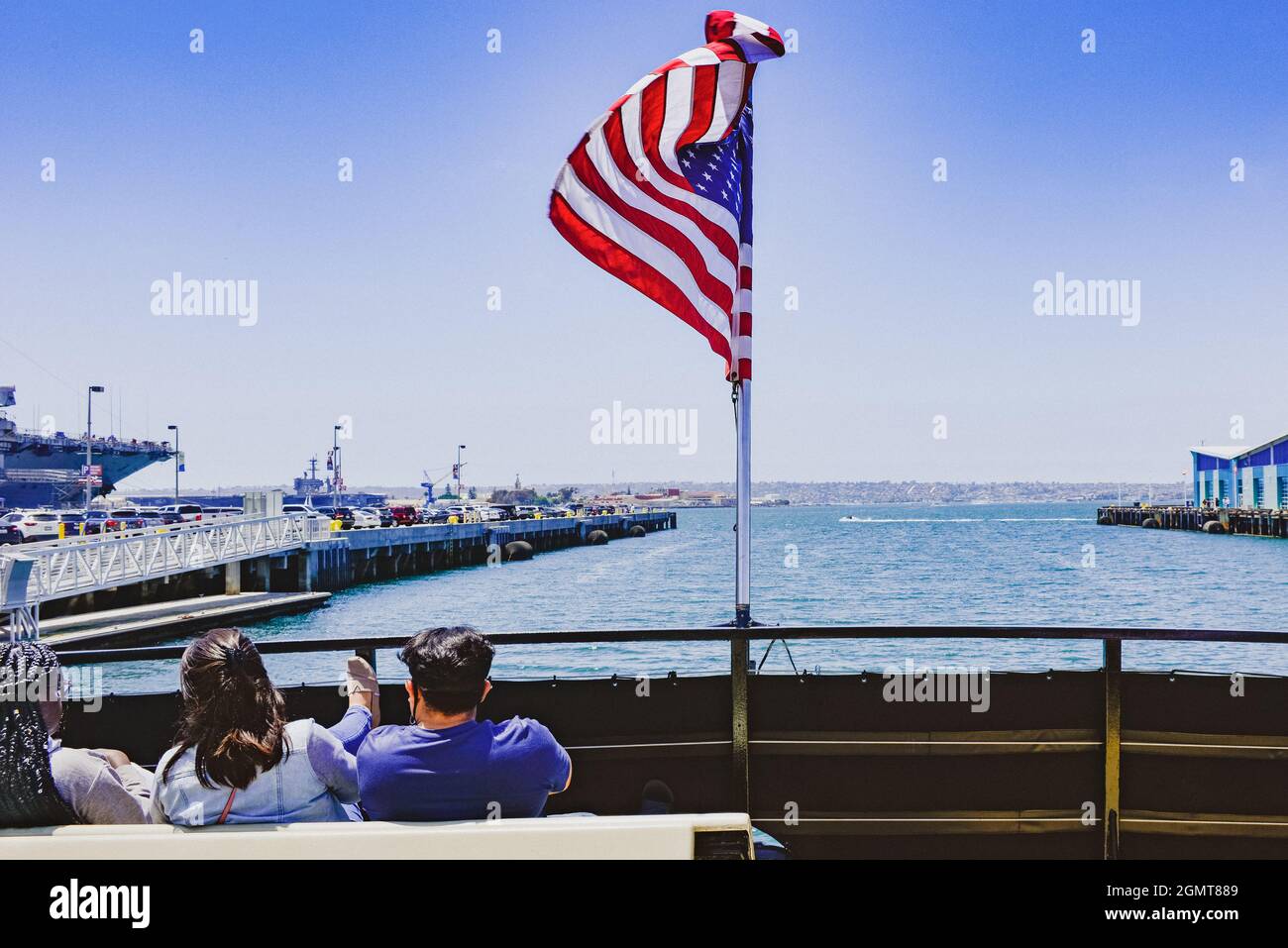 Rear view of Tourists seated on benches at the stern of a ferry boat with American flag flying with view of the San Diego Bay in San Diego, CA Stock Photo