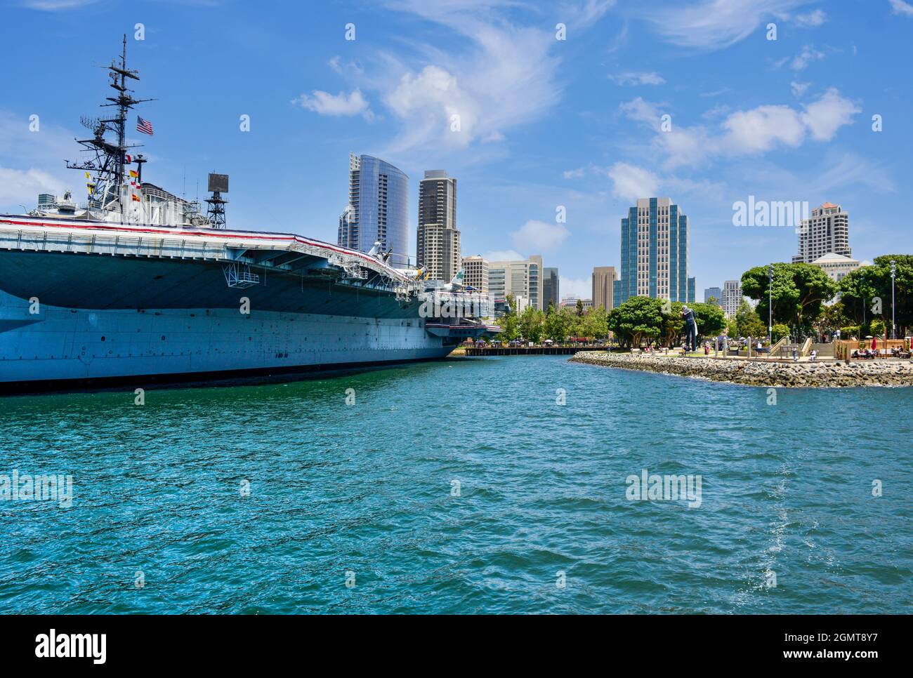 The historical USS Midway aircraft carrier, now retired as a museum at the harbor, with modern San Diego high-rise buildings nearby in San Diego, CA Stock Photo
