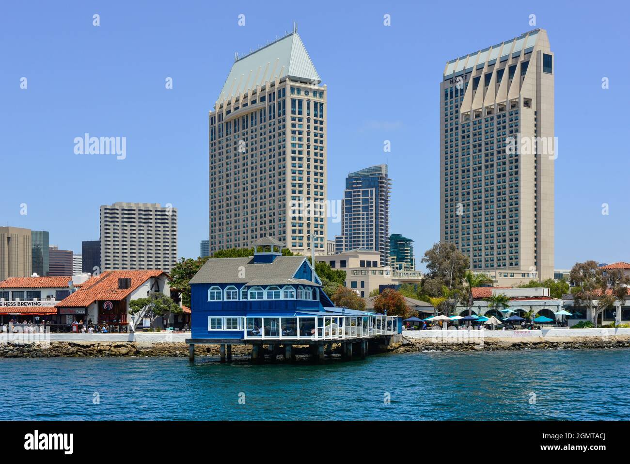The San Diego Pier restaurant in blue and white retro style on stilts in Seaport Village, with looming high-rise buildings on bay of San Diego, CA Stock Photo