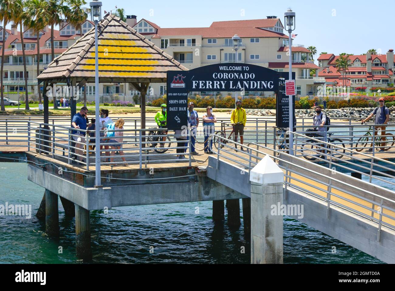 People, some on bicycles, await at the ferry loading pier for the Coronado Ferry boat arrival for travel across the San Diego Bay to San Diego Pier Stock Photo