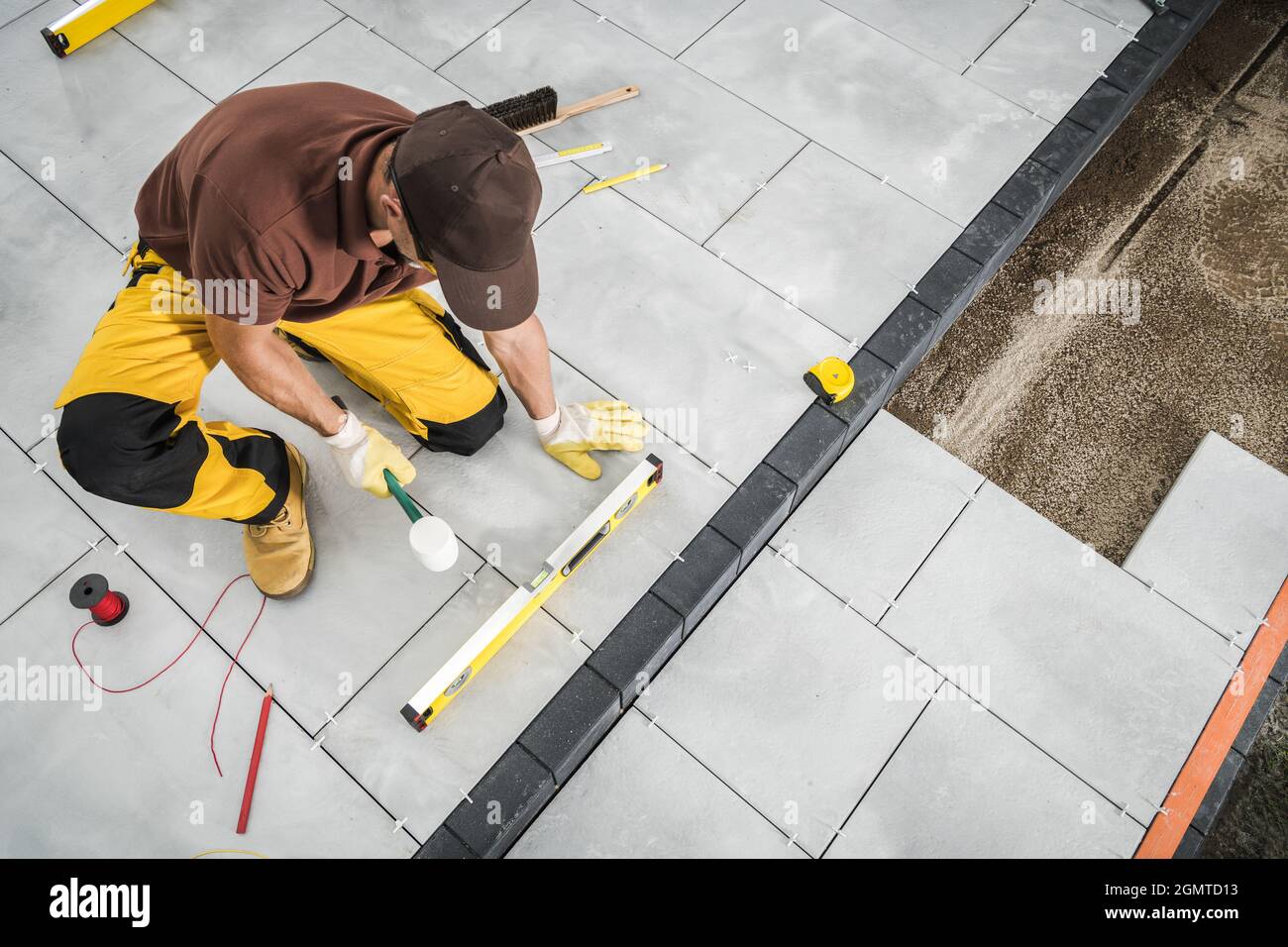 Professional Caucasian Worker Installing Concrete Paving Bricks Patio Floor. Industrial Theme. Stock Photo