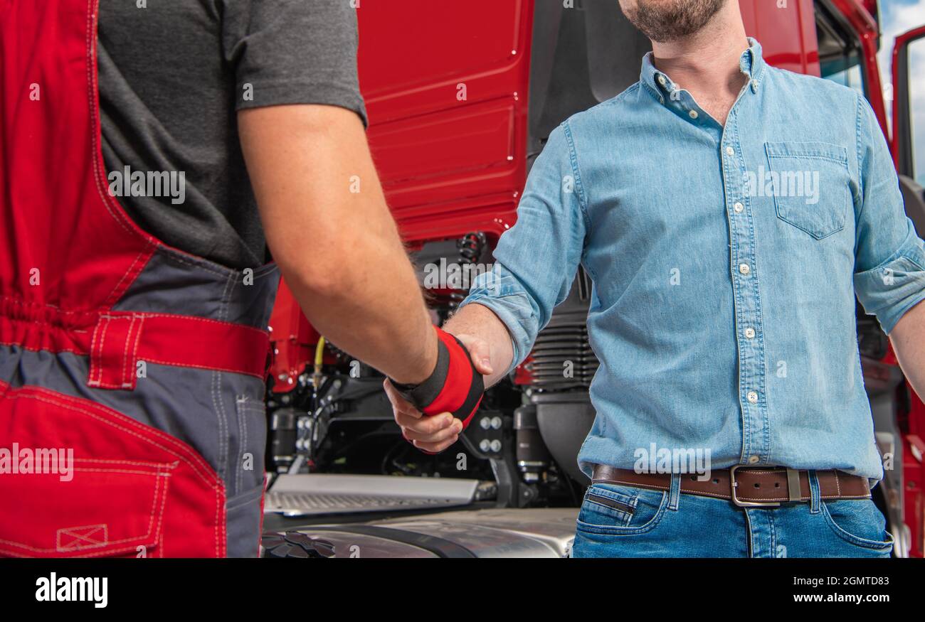 Truck Driver and His Mechanic Hand Shaking in Front of Modern Semi Truck Tractor. Heavy Transportation Industry Theme. Stock Photo