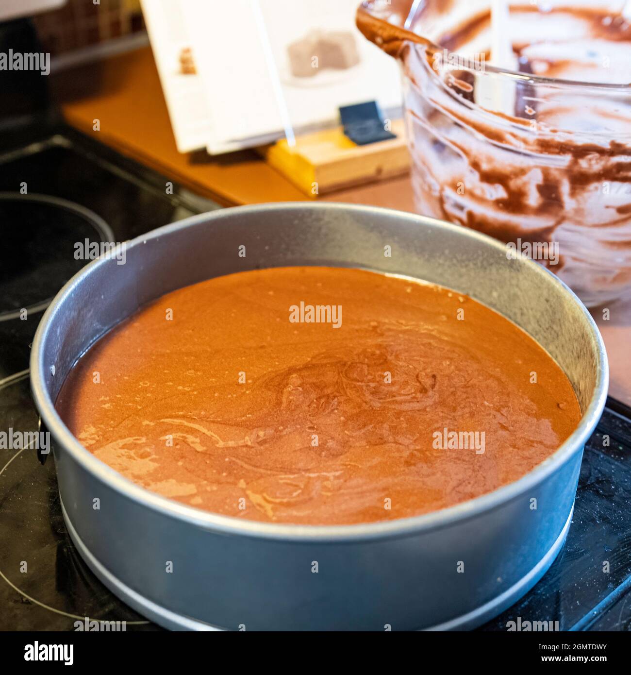 https://c8.alamy.com/comp/2GMTDWY/chocolate-cake-batter-in-a-metal-springform-pan-with-empty-glass-mixing-bowl-and-cookbook-in-background-out-of-focus-2GMTDWY.jpg