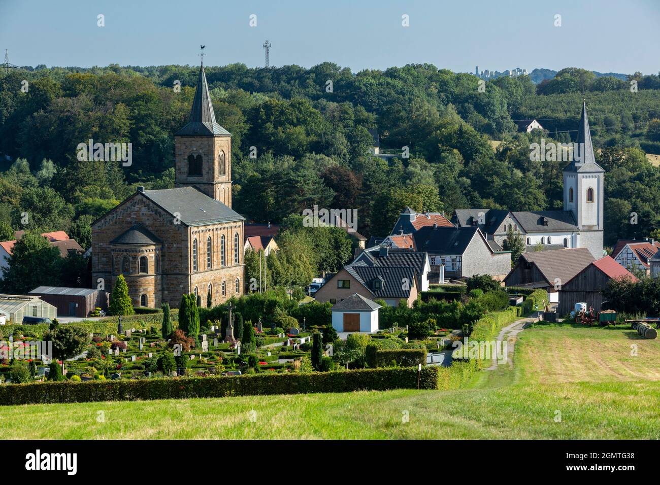 Germany, Wuelfrath, Wuelfrath-Duessel, Bergisches Land, Niederbergisches Land, Niederberg, Rhineland, North Rhine-Westphalia, NRW, panoramic view to Duessel village and the hilly landscape, ahead the cemetery, left the evangelic church, right the catholic church Saint Maximin, Romanesque, pillar basilica Stock Photo