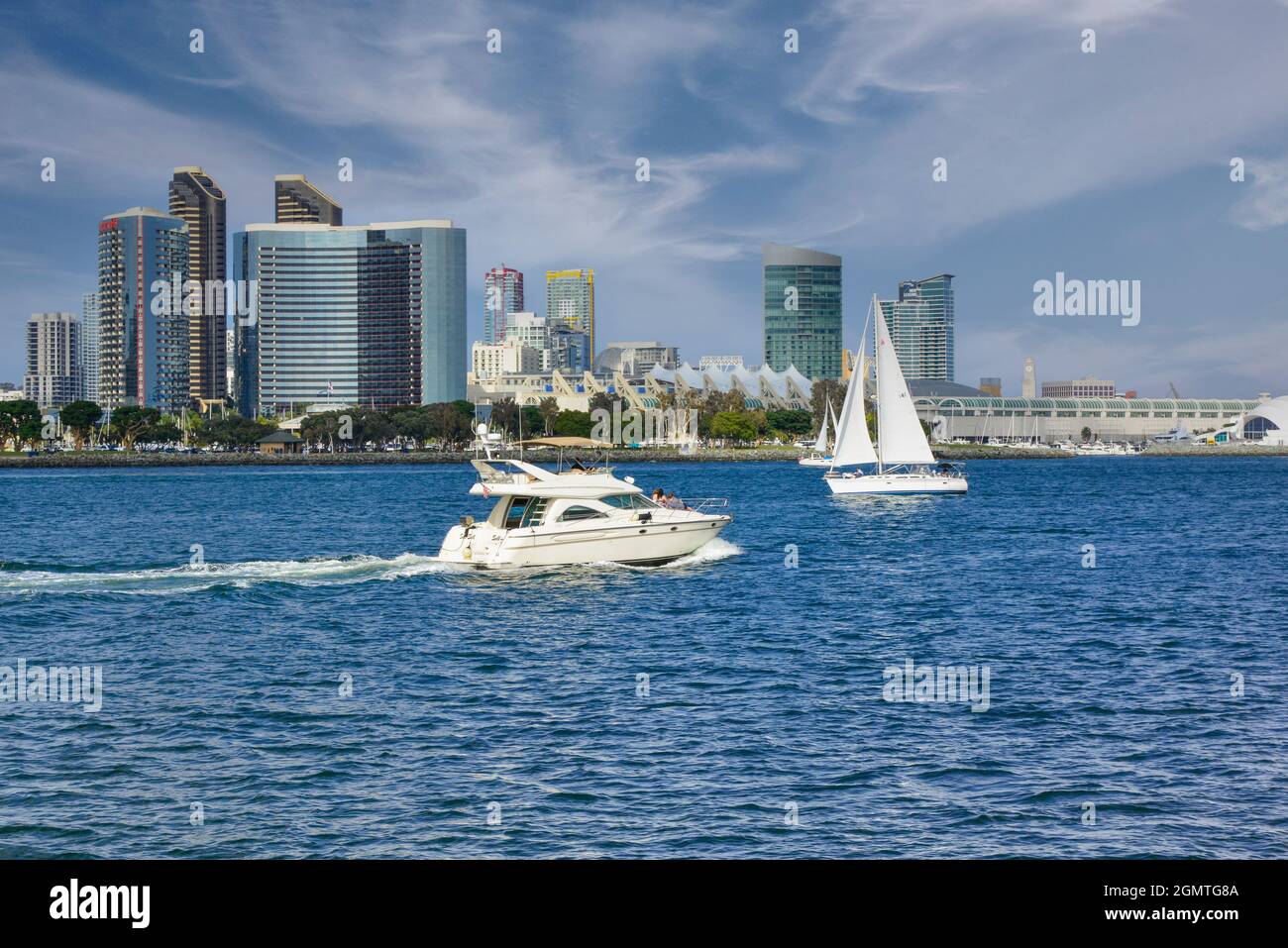 A speeding cabin cruiser boat along side sailboats leisurely sailing on the blue water bay before an impressive San Diego skyline in Southern CA Stock Photo