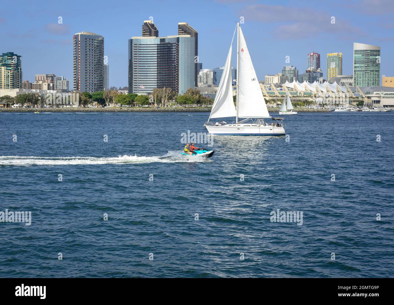 A speeding jet ski along side sailboats leisurely sailing on the blue water bay before an impressive San Diego skyline in Southern California Stock Photo