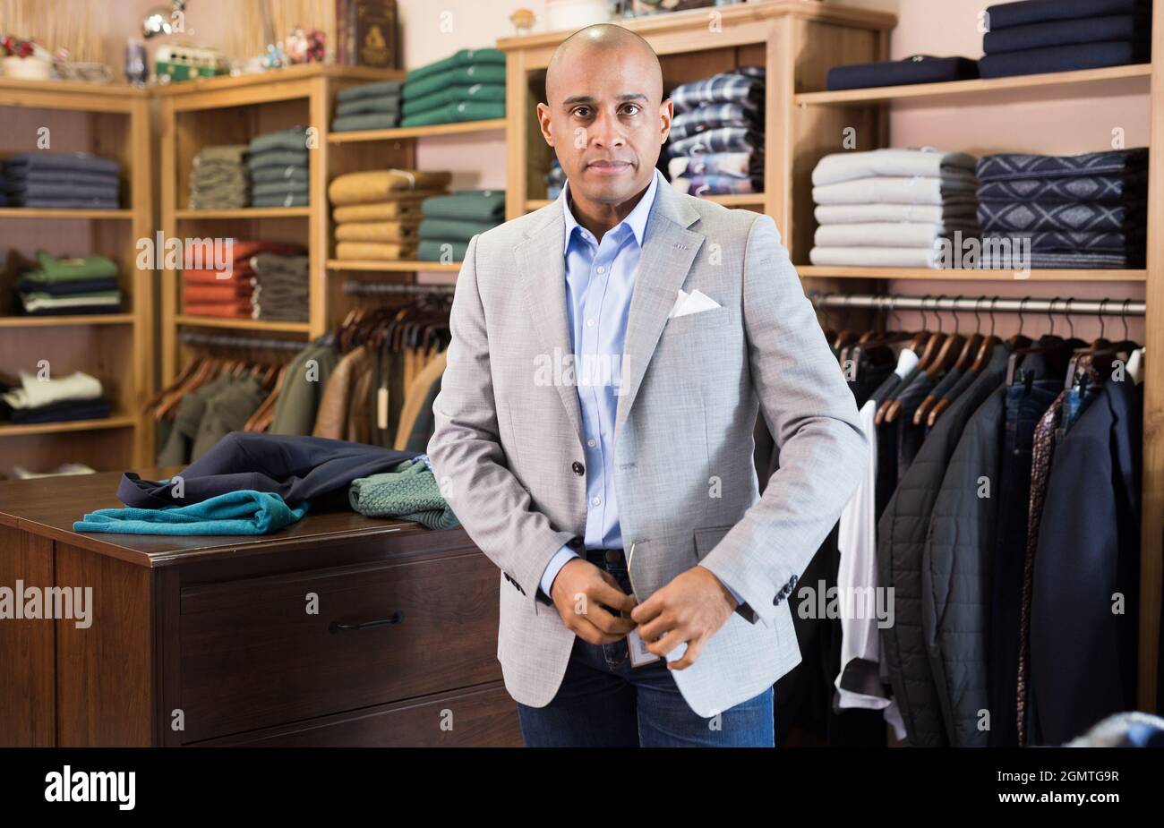 Portrait of young adult man choosing suit jacket in clothing store ...