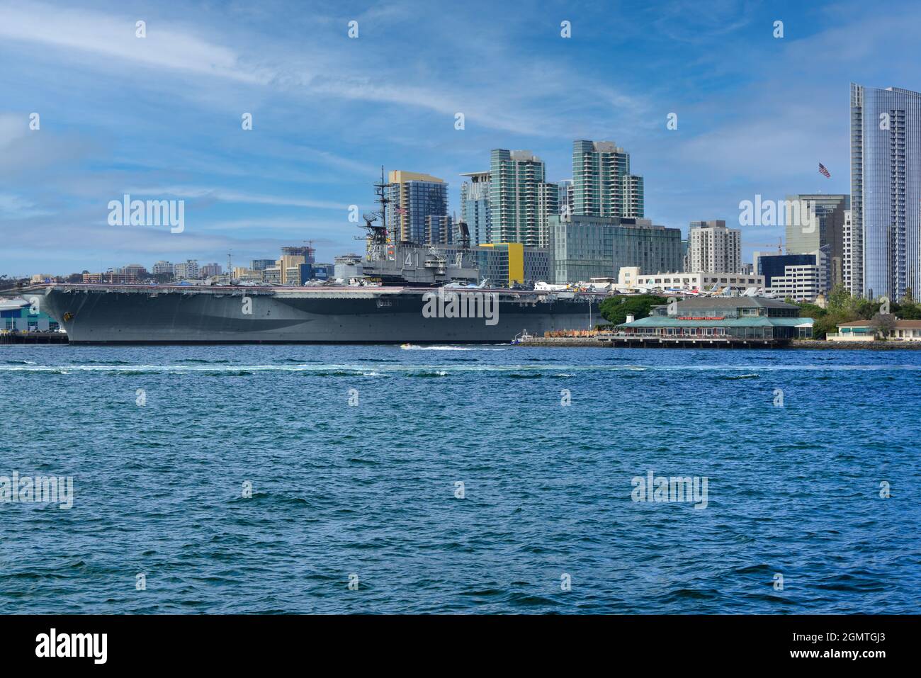 The USS Midway, the historical aircraft carrier battleship, now a museum,  at the San Diego Harbor with downtown San Diego skyline in background Stock Photo
