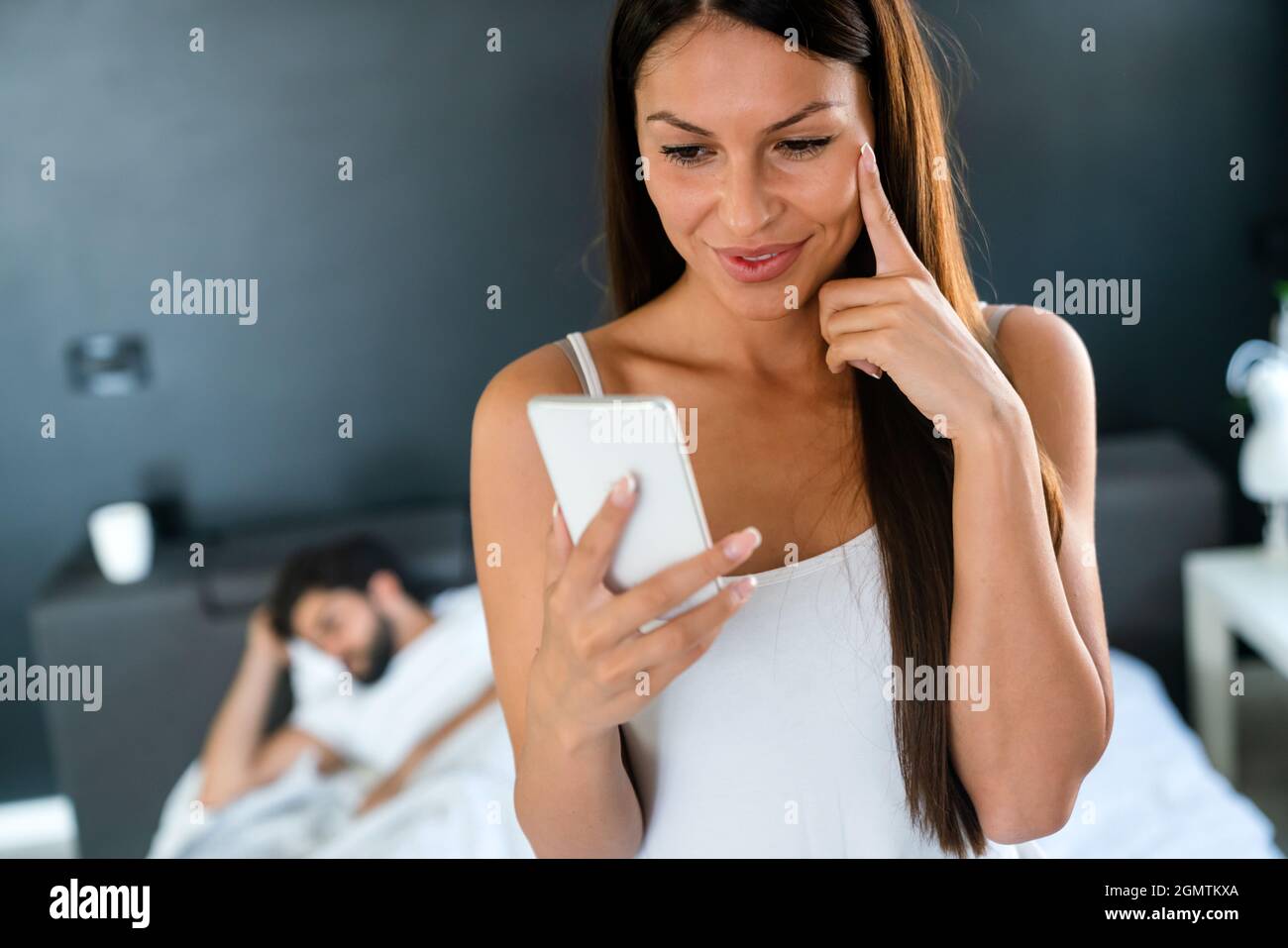 Woman talking privately on cellphone while her husband sleeping on bed Stock Photo