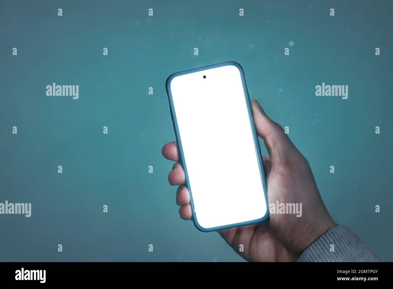 Hand holding a glowing smartphone with a blank screen Stock Photo