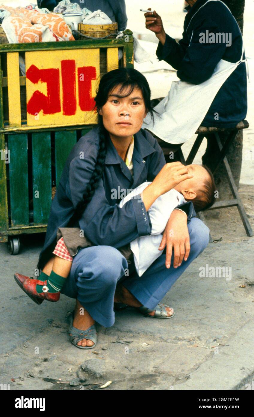 Guilin, China - August 1981; In 1981, when I took this shot of a squatting ethnic woman holding her baby in a Guilin market, China was just opening up Stock Photo