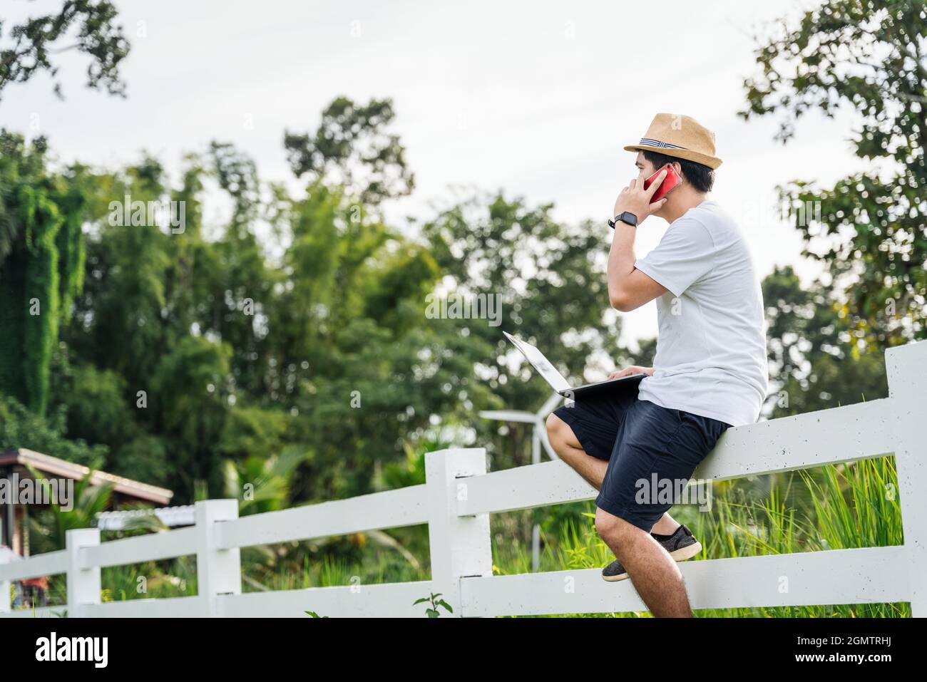 Asian young man traveler using laptop computer while enjoying beautiful tropical in nature. Freelancer guy working on freelance on netbook during vaca Stock Photo
