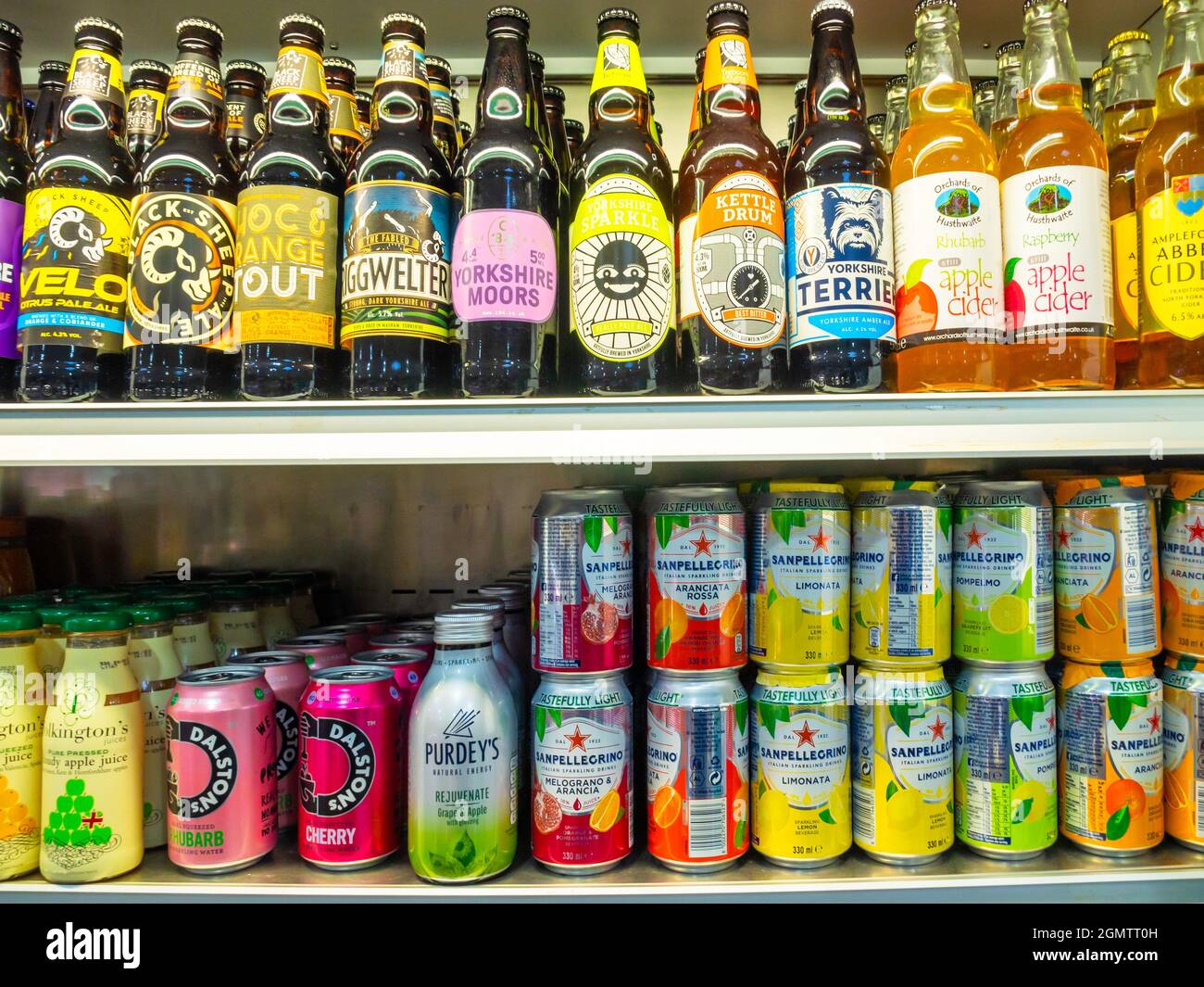 Local bottled Yorkshire beer and cider and  San Pellegrino Italian soft drink cans displayed on a shelves in a small grocers shop Stock Photo