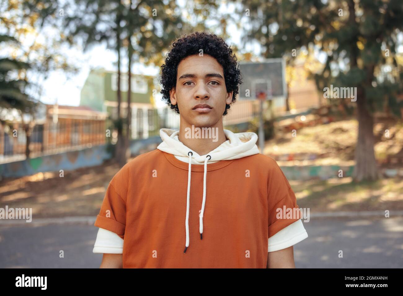 Confident male youngster looking at the camera outdoors. Teenage boy wearing casual clothing in an urban park. Self-confident young teenager standing Stock Photo