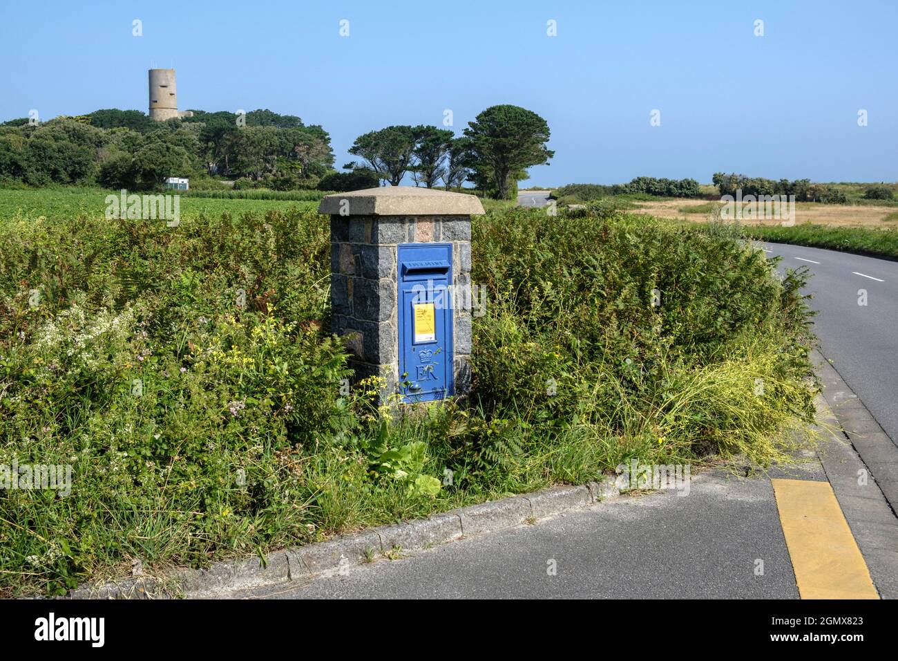 The Lihou Island post box at L'Erée looking towards the tower of Fort Saumarez, Guernsey.  Les Sablons, L'Erée, Guernsey, Channel Islands. Stock Photo