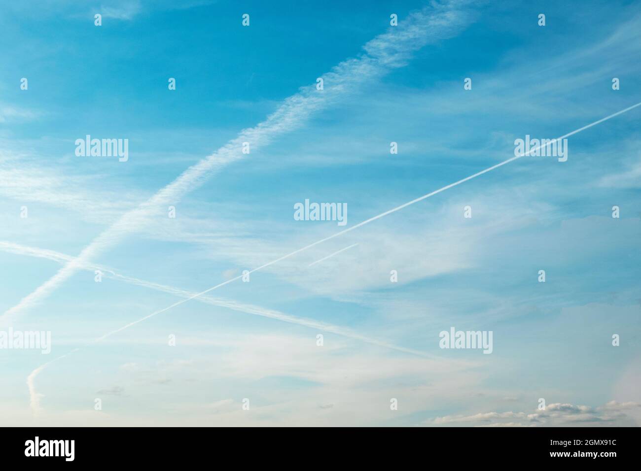 White crisscrossing trails of airplanes, traces of planes on blue sky as background Stock Photo