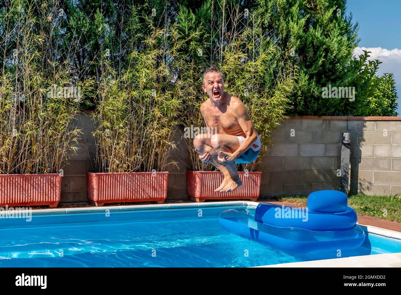 Middle-aged white man dives into a pool, cannonball style, while screaming like crazy and jumping over an airbed Stock Photo