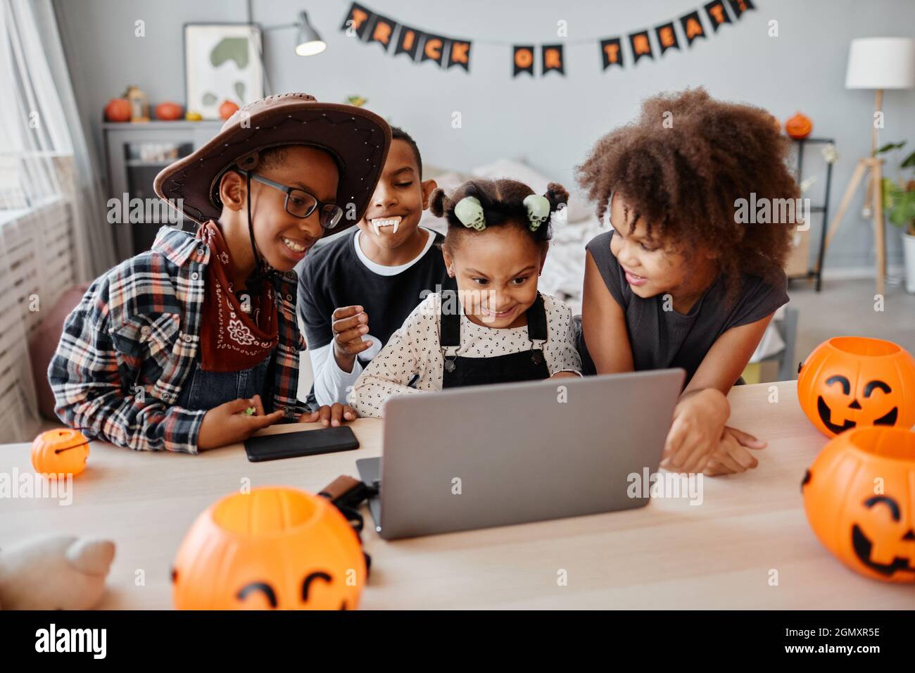Portrait of happy African-American kids wearing Halloween costumes while using laptop at home and video chatting with family online, copy space Stock Photo