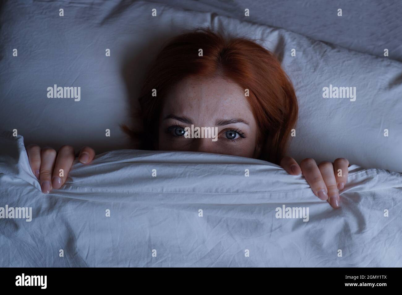 sleepless woman lying in bed hiding under duvet at night Stock Photo