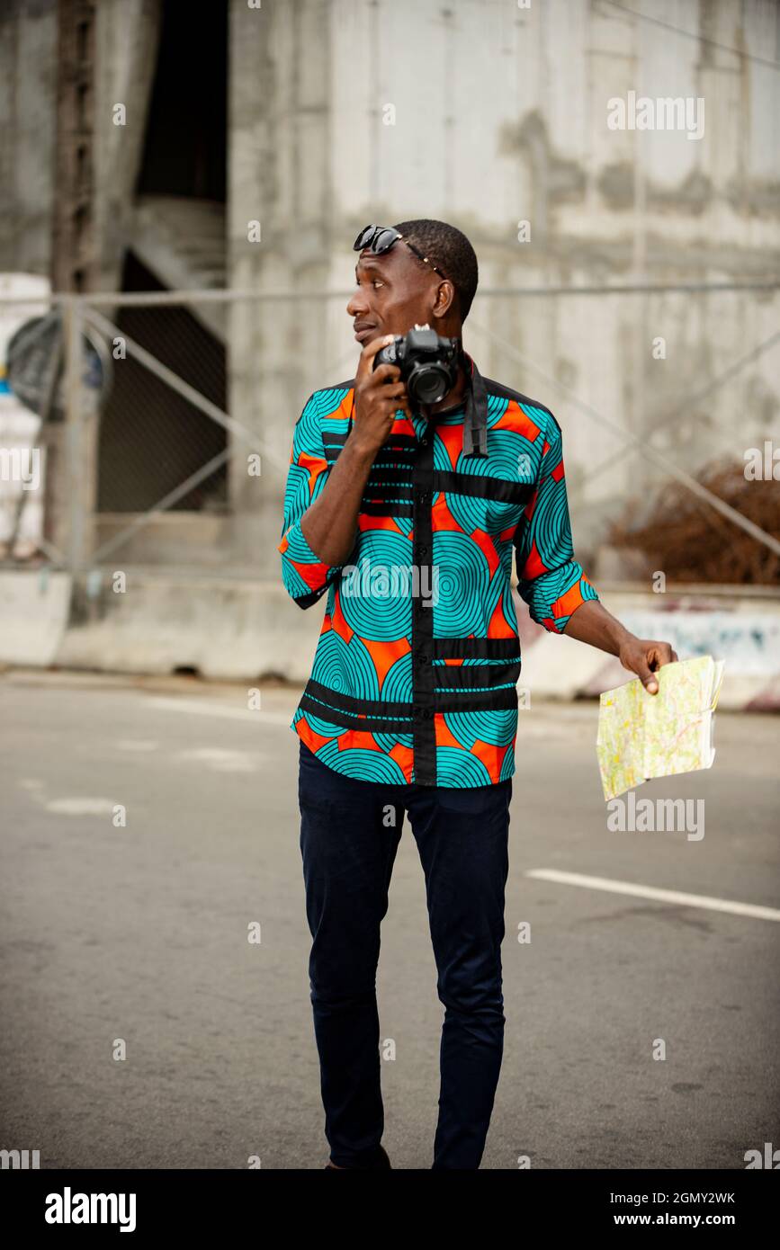 pretty young man tourist standing outside holding a camera and a map look aside Stock Photo
