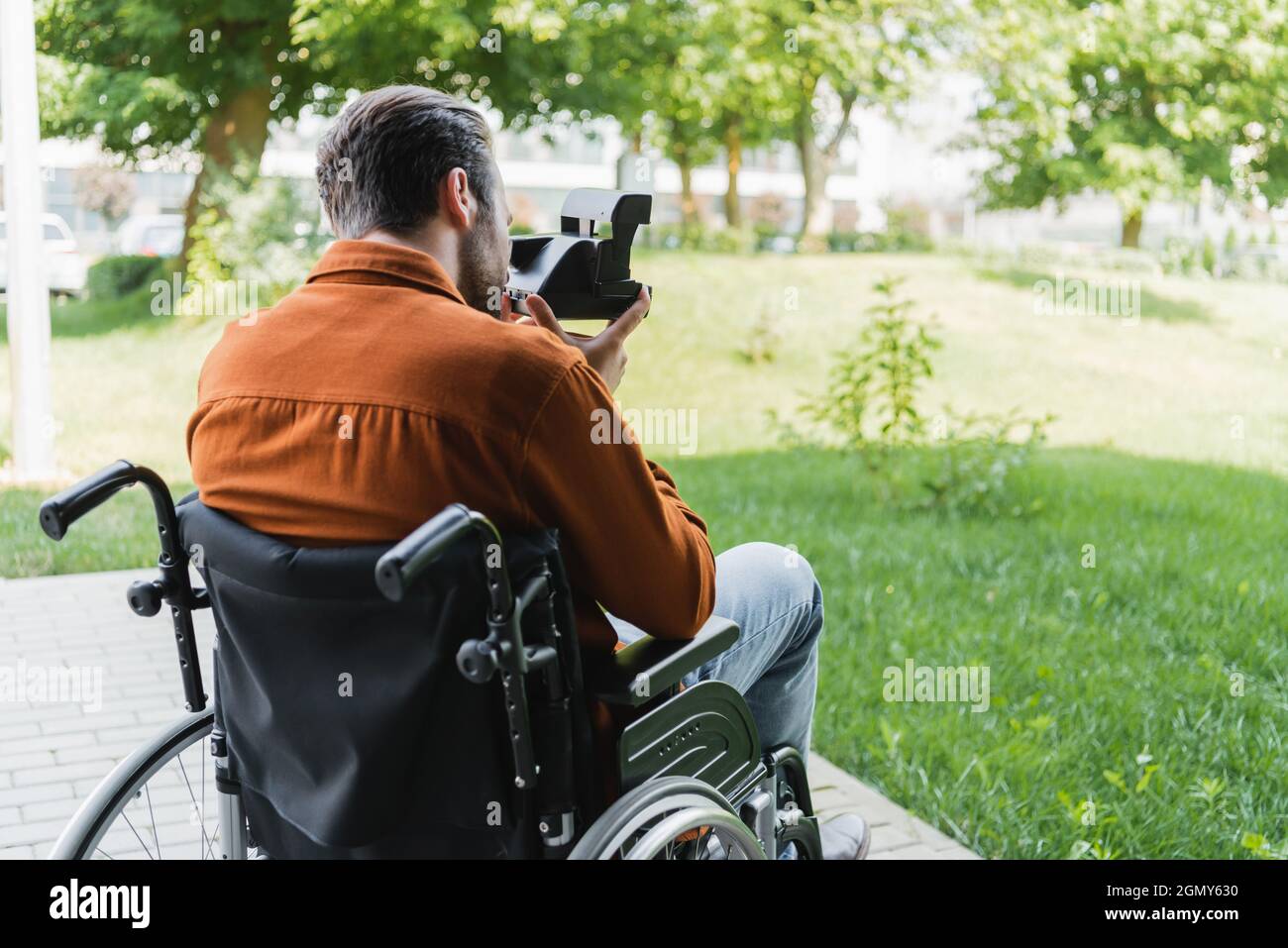 back view of handicapped man in wheelchair taking photo on vintage camera outdoors Stock Photo