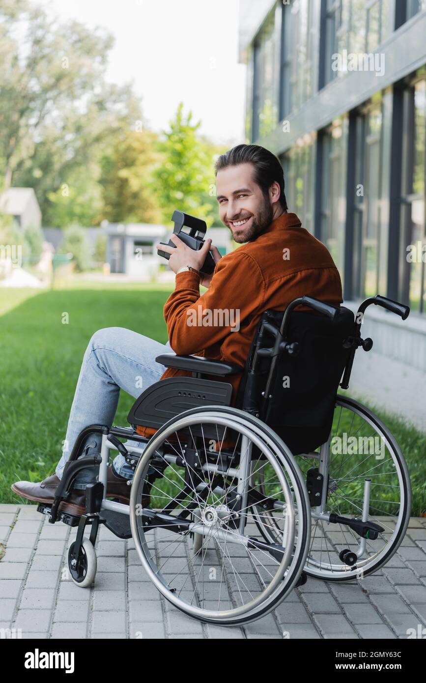 happy disabled man in wheelchair smiling at camera while holding vintage camera Stock Photo