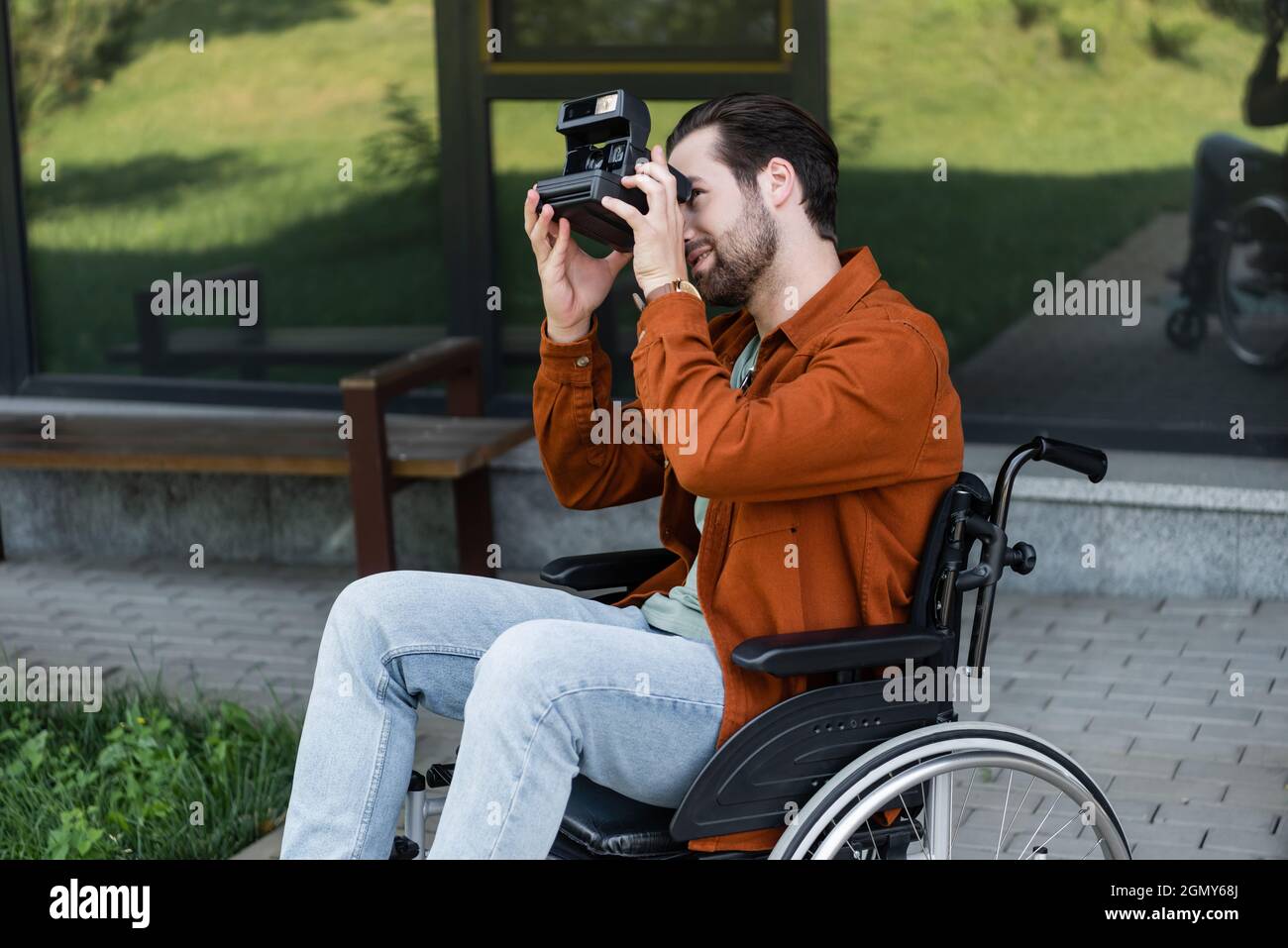 handicapped man in wheelchair taking picture on vintage camera outdoors Stock Photo