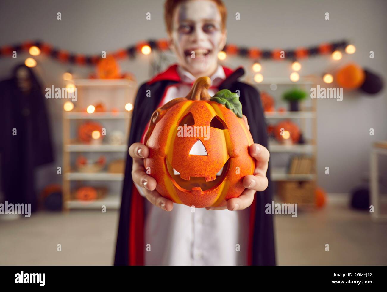 Close up of small Halloween pumpkin in hands of little boy who is disguised as vampire. Stock Photo