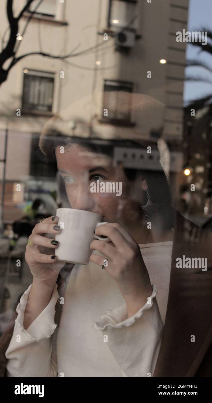 Young woman drinking a hot cup of coffee in cafeteria. Parisian Vibes Style for Autumn Season 2021. Stock Photo