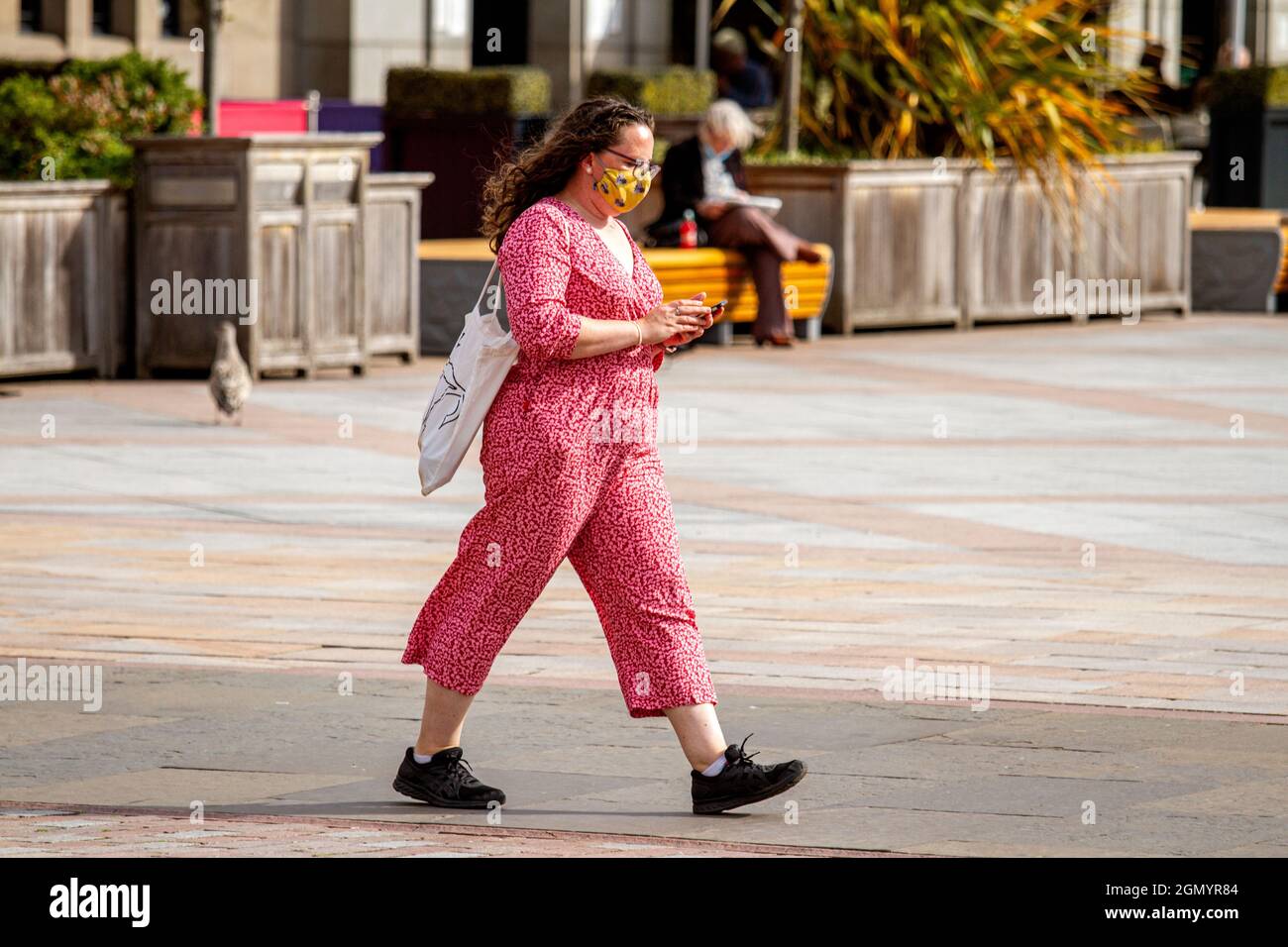 Dundee, Tayside, Scotland, UK. 21st. September 2021. UK weather: A sunny day with a strong cool  breeze across North East Scotland, temperatures reaching 17°C. A fashionable woman wearing a facemask and a pink colourful all in one outfit spending the day out enjoying the cool sunny weather whilst texting messages on her mobile phone in Dundee city centre. Credit: Dundee Photographics/Alamy Live News Stock Photo