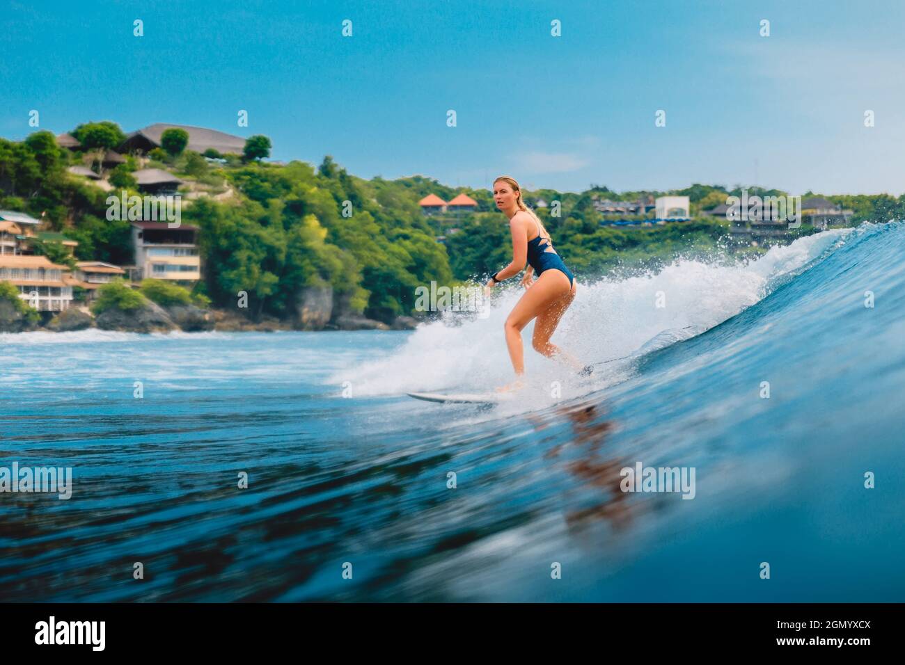 Surf girl at surfboard on blue wave in Bali, Impossibles beach. Sporty