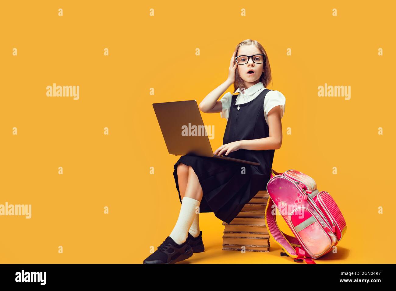 Full length surprised pupil sit on the stack of books with laptop Look ...