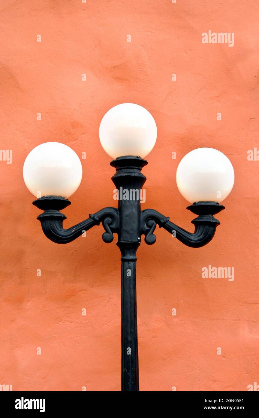 Black iron lamp stand holds three round white, light globes. It stands
