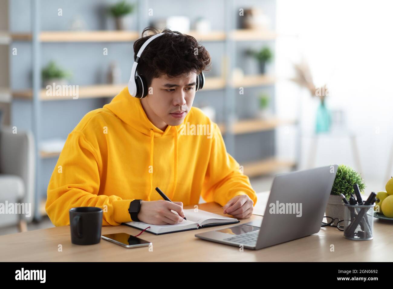 Focused asian man working on laptop and writing Stock Photo