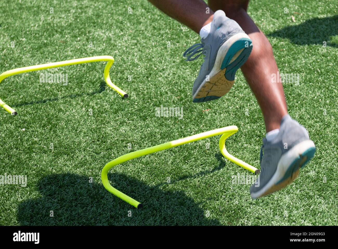 Male athlete jumping over yellow mini hurdles on a green turf field close up with motion blur showing the speed of the dports drill. Stock Photo